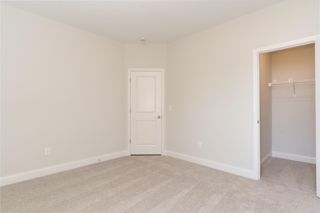 unfurnished bedroom featuring light colored carpet, a spacious closet, baseboards, and a closet