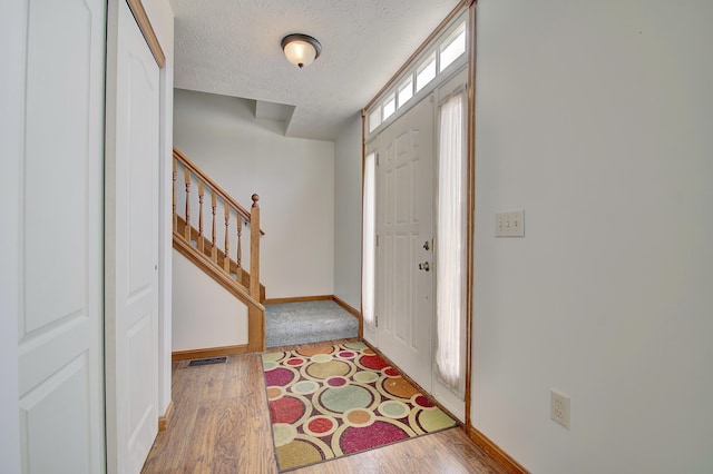 foyer entrance featuring a textured ceiling, wood finished floors, stairs, and baseboards