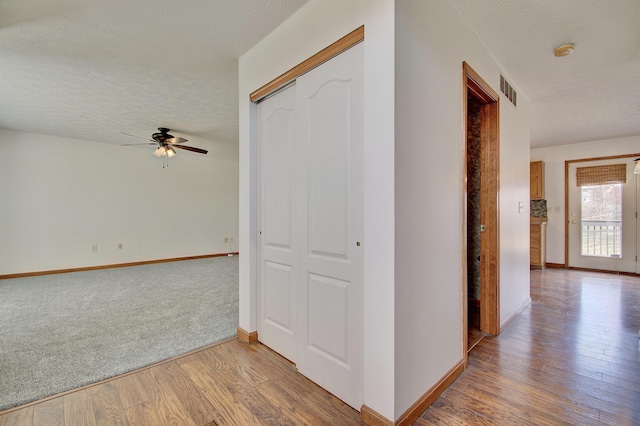 hall featuring visible vents, a textured ceiling, baseboards, and wood finished floors