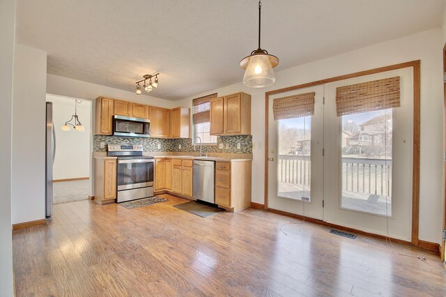 kitchen with light wood-style flooring, stainless steel appliances, a sink, visible vents, and decorative backsplash