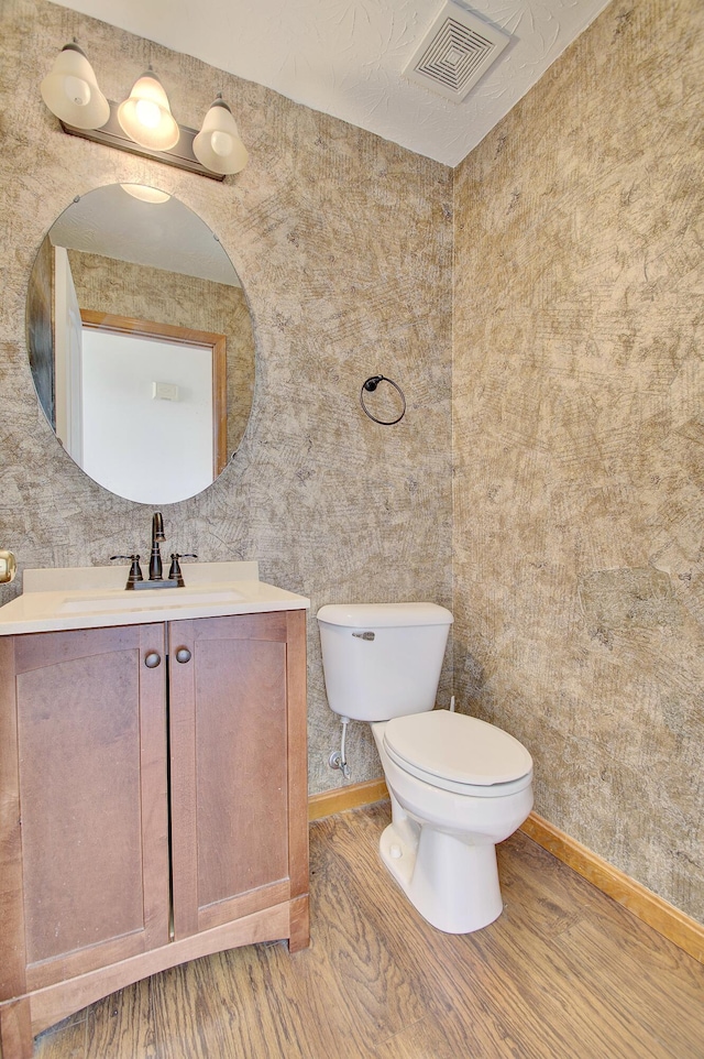 half bath featuring toilet, vanity, visible vents, and baseboards