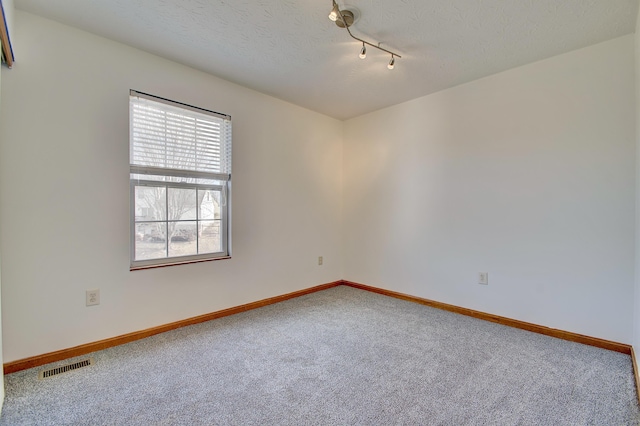 empty room with a textured ceiling, carpet flooring, visible vents, and baseboards