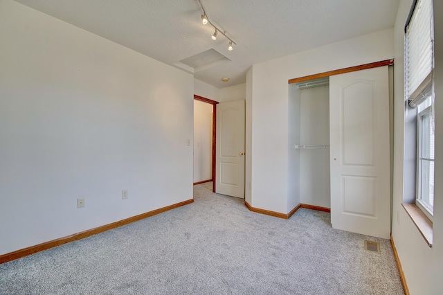 unfurnished bedroom featuring light carpet, attic access, visible vents, baseboards, and a closet