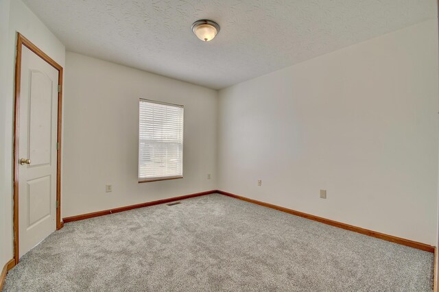 carpeted spare room with visible vents, a textured ceiling, and baseboards