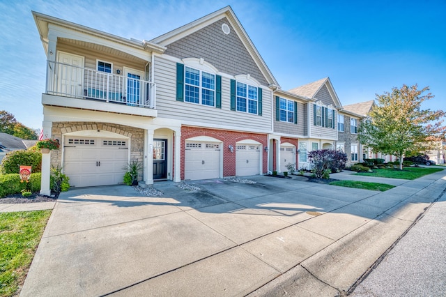 townhome / multi-family property featuring an attached garage, a balcony, brick siding, driveway, and stone siding