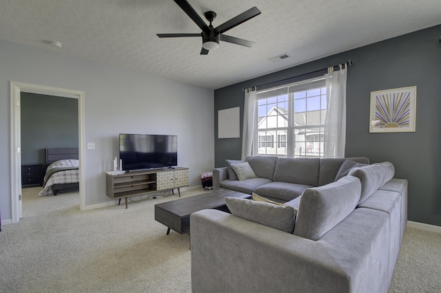 carpeted living area featuring baseboards, a textured ceiling, visible vents, and a ceiling fan