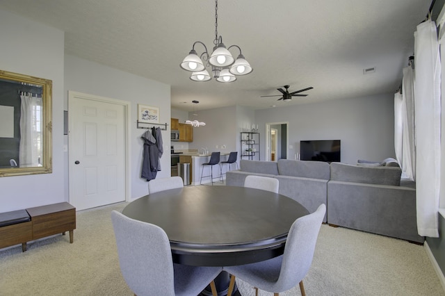 dining area with light carpet, a textured ceiling, ceiling fan with notable chandelier, and visible vents