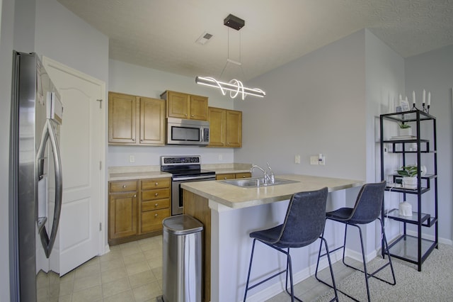 kitchen with brown cabinetry, a breakfast bar, stainless steel appliances, light countertops, and a sink