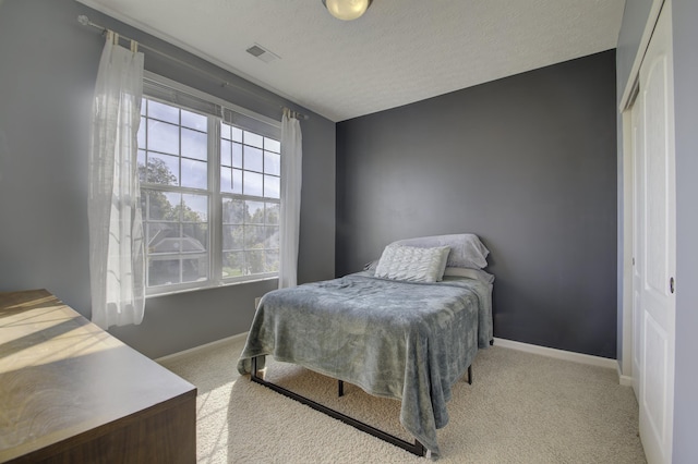 carpeted bedroom featuring a textured ceiling, a closet, visible vents, and baseboards