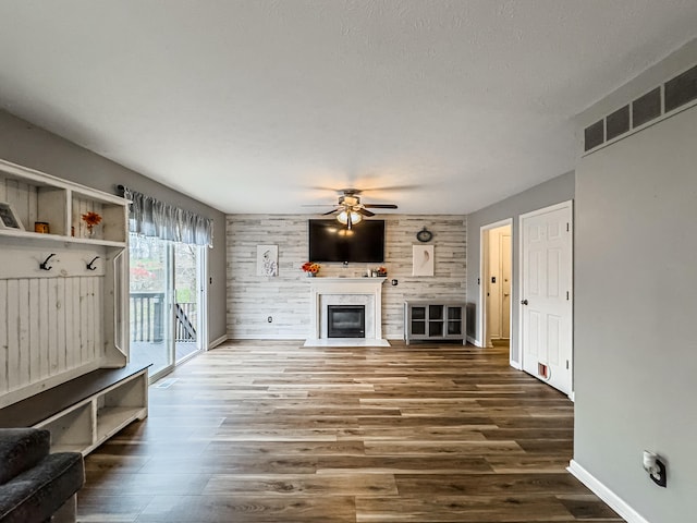 unfurnished living room featuring wooden walls, ceiling fan, dark wood-type flooring, and a textured ceiling