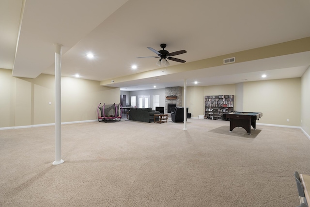 playroom featuring a stone fireplace, light carpet, and ceiling fan