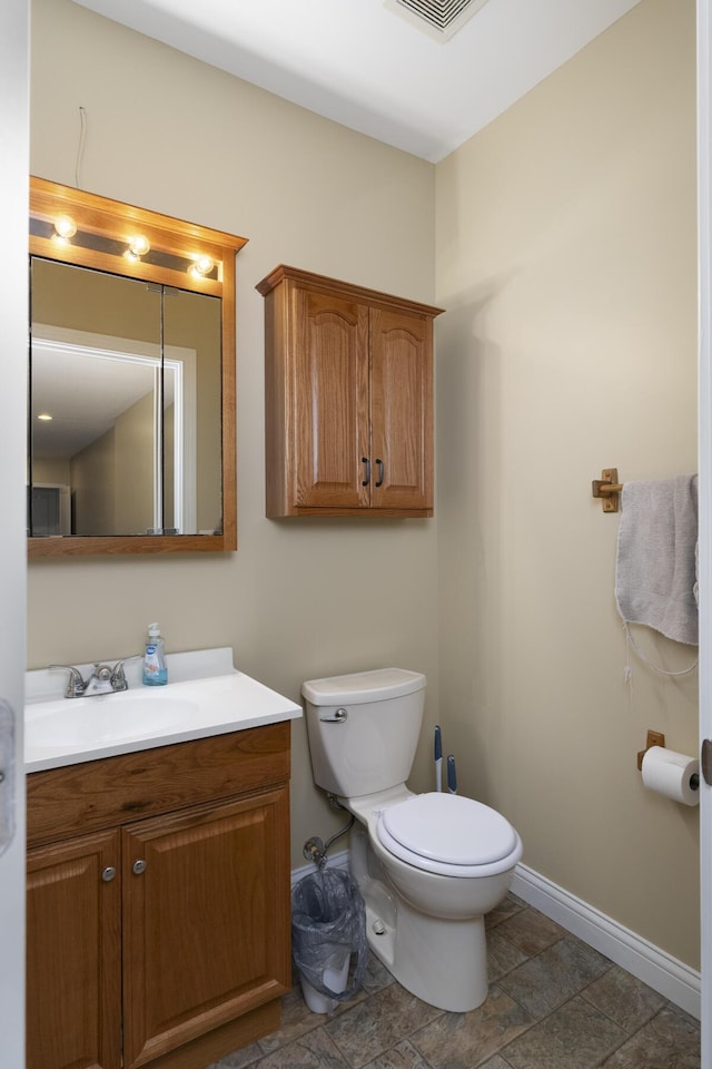 bathroom with vanity, visible vents, baseboards, stone finish flooring, and toilet