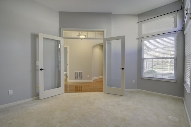 unfurnished bedroom featuring light carpet, french doors, and a high ceiling