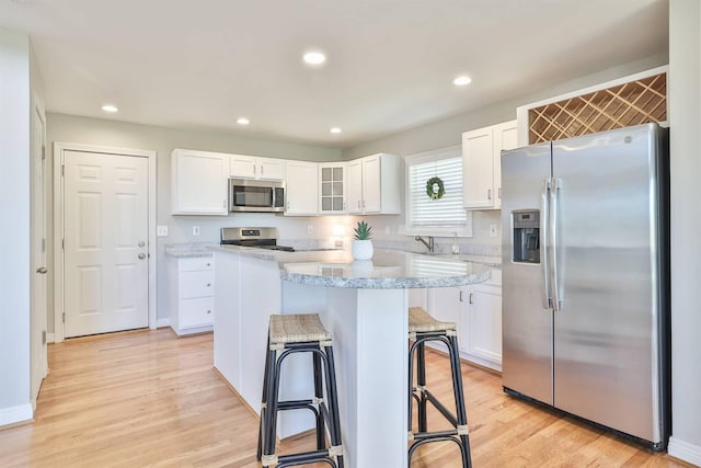 kitchen featuring a breakfast bar, a center island, white cabinets, light wood-type flooring, and appliances with stainless steel finishes