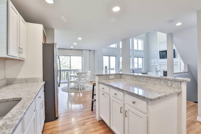 kitchen with stainless steel fridge, white cabinets, and light hardwood / wood-style floors