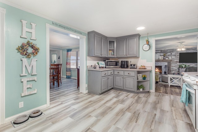 kitchen with gray cabinetry, light countertops, ornamental molding, stainless steel microwave, and glass insert cabinets