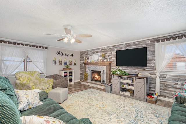 living area with a textured ceiling, ceiling fan, a fireplace, wood finished floors, and ornamental molding