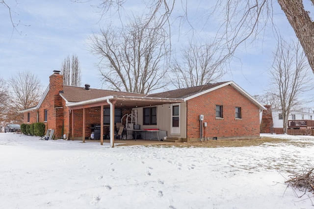 snow covered property with covered porch, brick siding, and a chimney