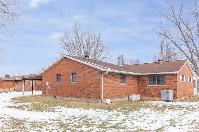 snow covered property with roof with shingles, central AC unit, and brick siding