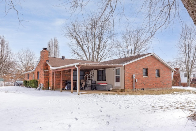 snow covered house with a chimney, a porch, and brick siding