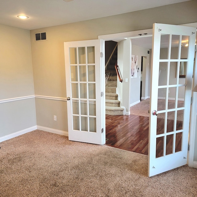 empty room with carpet floors, visible vents, baseboards, french doors, and stairway