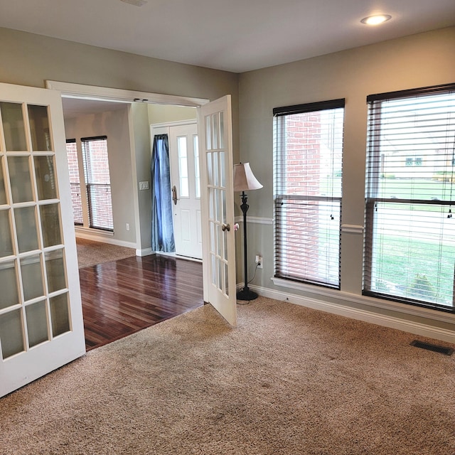 carpeted empty room featuring baseboards, visible vents, a wealth of natural light, and french doors