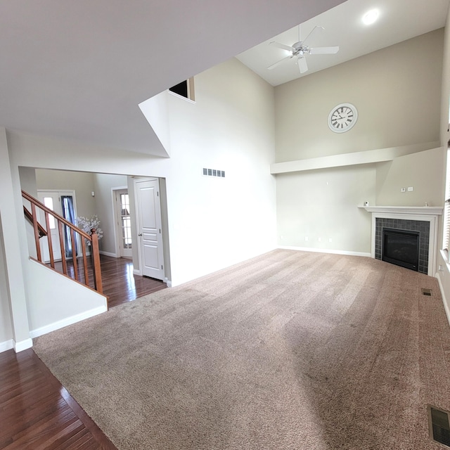 unfurnished living room with stairs, a towering ceiling, a tile fireplace, and visible vents