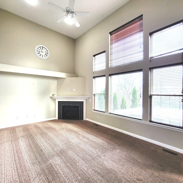 unfurnished living room with baseboards, visible vents, a tile fireplace, a high ceiling, and carpet floors