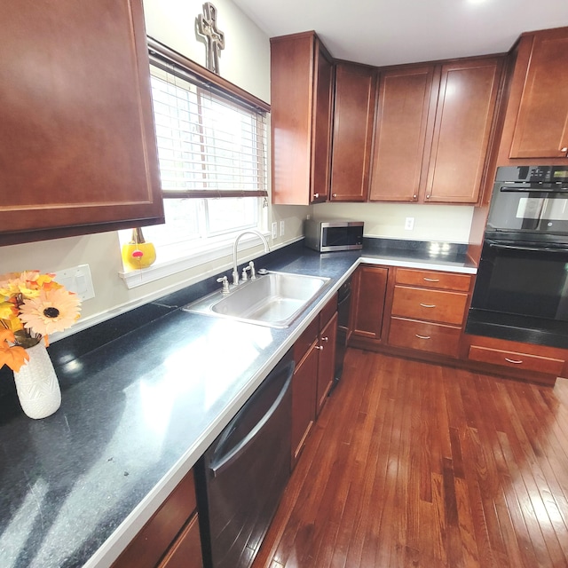 kitchen featuring appliances with stainless steel finishes, dark countertops, a sink, and dark wood-style floors