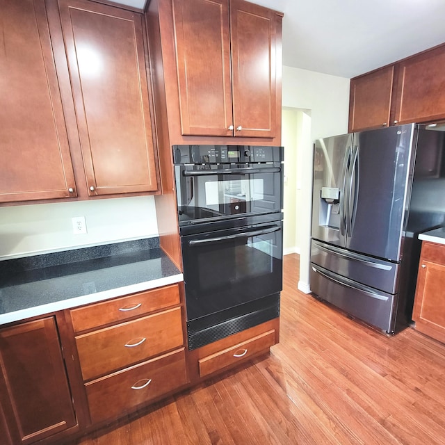 kitchen featuring dark countertops, dobule oven black, light wood finished floors, and stainless steel fridge with ice dispenser