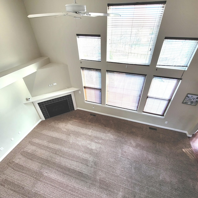 unfurnished living room featuring a ceiling fan, baseboards, carpet flooring, and a high ceiling