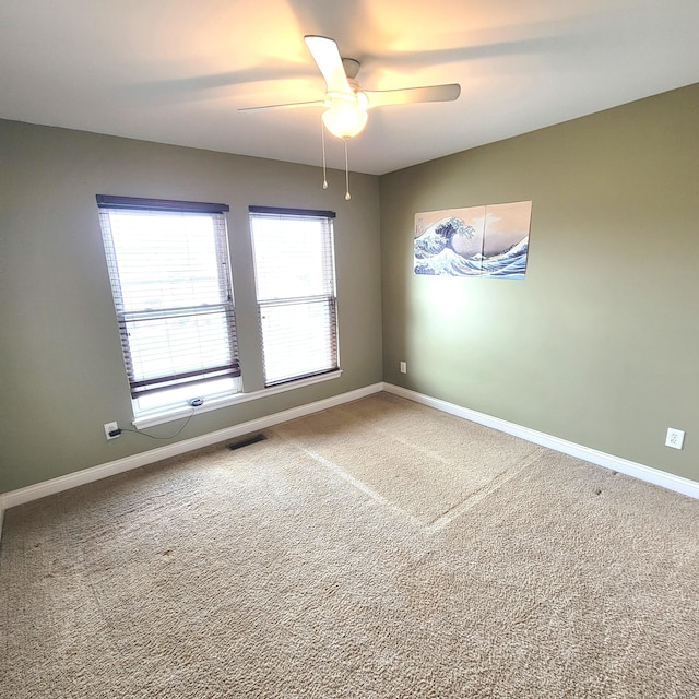 carpeted empty room featuring a ceiling fan, visible vents, and baseboards