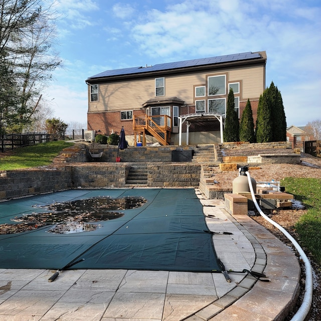 rear view of house featuring roof mounted solar panels, fence, and brick siding