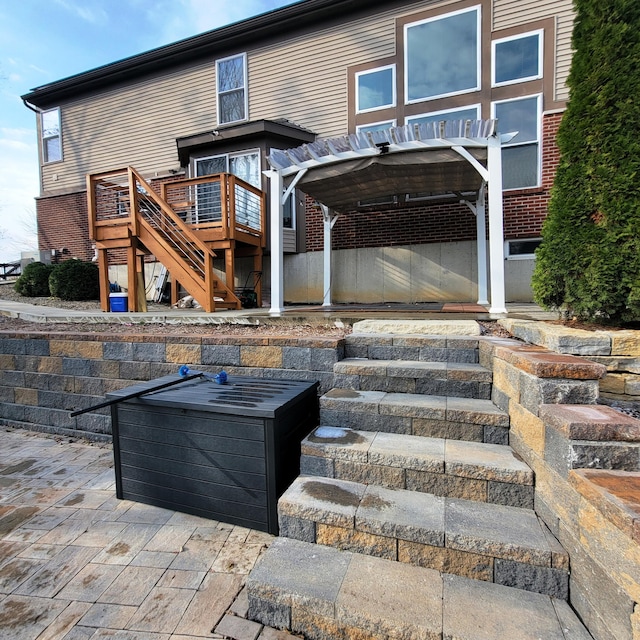 rear view of house featuring stairs, brick siding, and a patio area