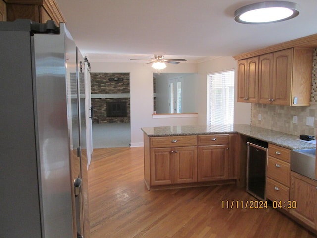 kitchen with ceiling fan, light stone counters, light hardwood / wood-style flooring, kitchen peninsula, and appliances with stainless steel finishes