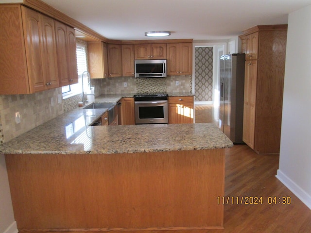 kitchen featuring kitchen peninsula, appliances with stainless steel finishes, light wood-type flooring, and sink