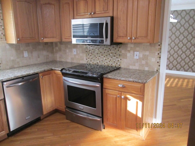 kitchen featuring backsplash, light stone countertops, stainless steel appliances, and light hardwood / wood-style floors