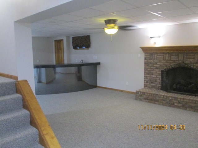 basement featuring carpet flooring, a paneled ceiling, ceiling fan, and a fireplace