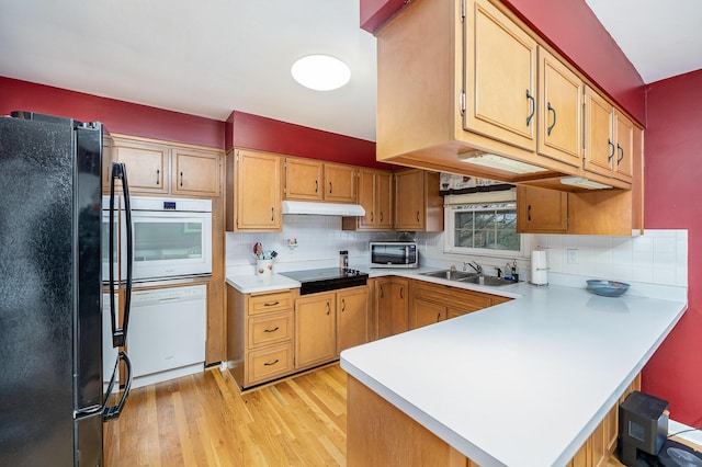 kitchen with kitchen peninsula, decorative backsplash, light wood-type flooring, sink, and black appliances