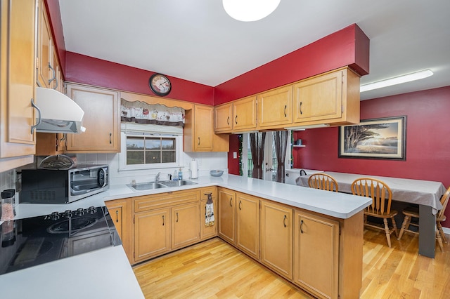 kitchen featuring kitchen peninsula, light wood-type flooring, range hood, and sink