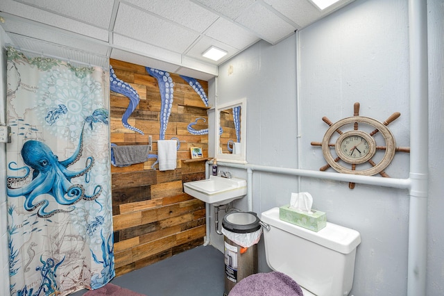 bathroom featuring toilet, a drop ceiling, and wood walls