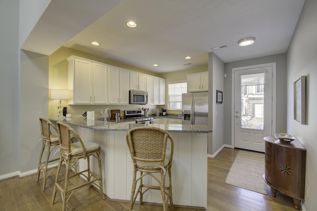 kitchen with light stone counters, kitchen peninsula, light hardwood / wood-style floors, white cabinets, and appliances with stainless steel finishes