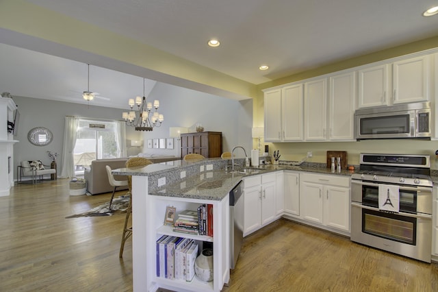 kitchen featuring white cabinetry, sink, stainless steel appliances, light stone counters, and kitchen peninsula