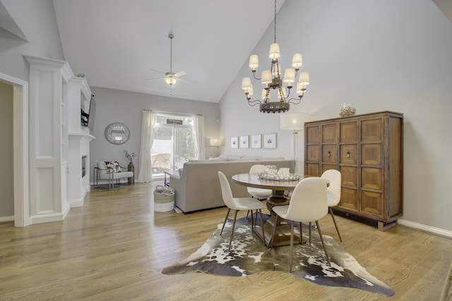 dining area featuring ceiling fan with notable chandelier, high vaulted ceiling, and light hardwood / wood-style flooring