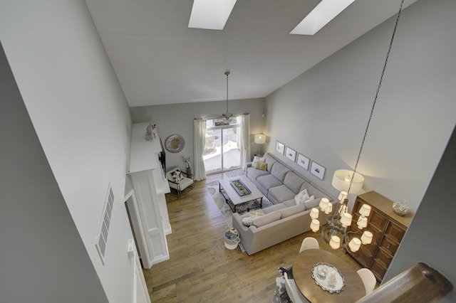 living room featuring vaulted ceiling with skylight, a notable chandelier, and wood-type flooring