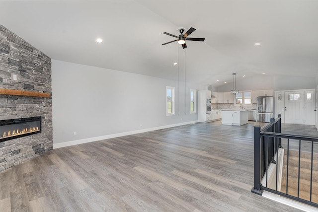 living room featuring light hardwood / wood-style flooring, vaulted ceiling, ceiling fan, and a stone fireplace