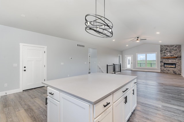 kitchen featuring a stone fireplace, white cabinets, vaulted ceiling, and light wood-type flooring