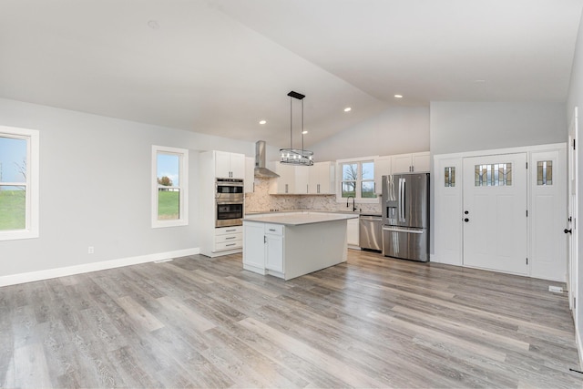 kitchen featuring a center island, wall chimney exhaust hood, decorative light fixtures, white cabinets, and appliances with stainless steel finishes