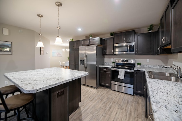 kitchen with stainless steel appliances, sink, pendant lighting, light hardwood / wood-style flooring, and a breakfast bar area