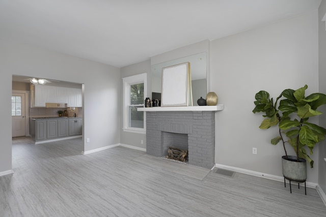 unfurnished living room with a healthy amount of sunlight, light wood-type flooring, and a brick fireplace